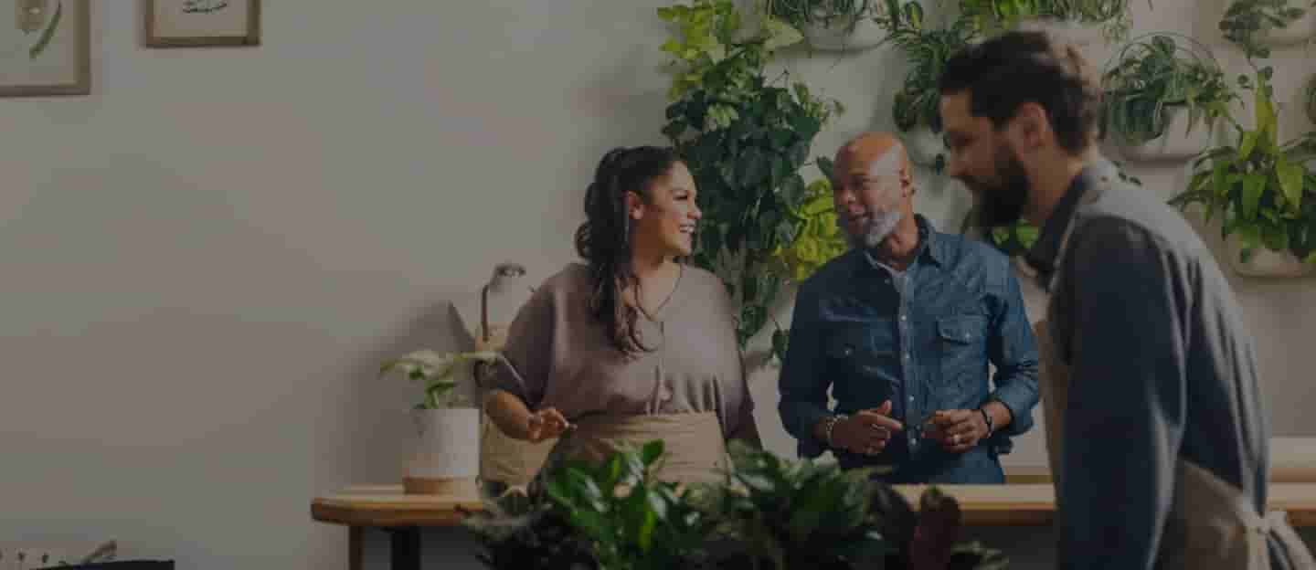 Shop owners smile and talk while an employee moves plants.