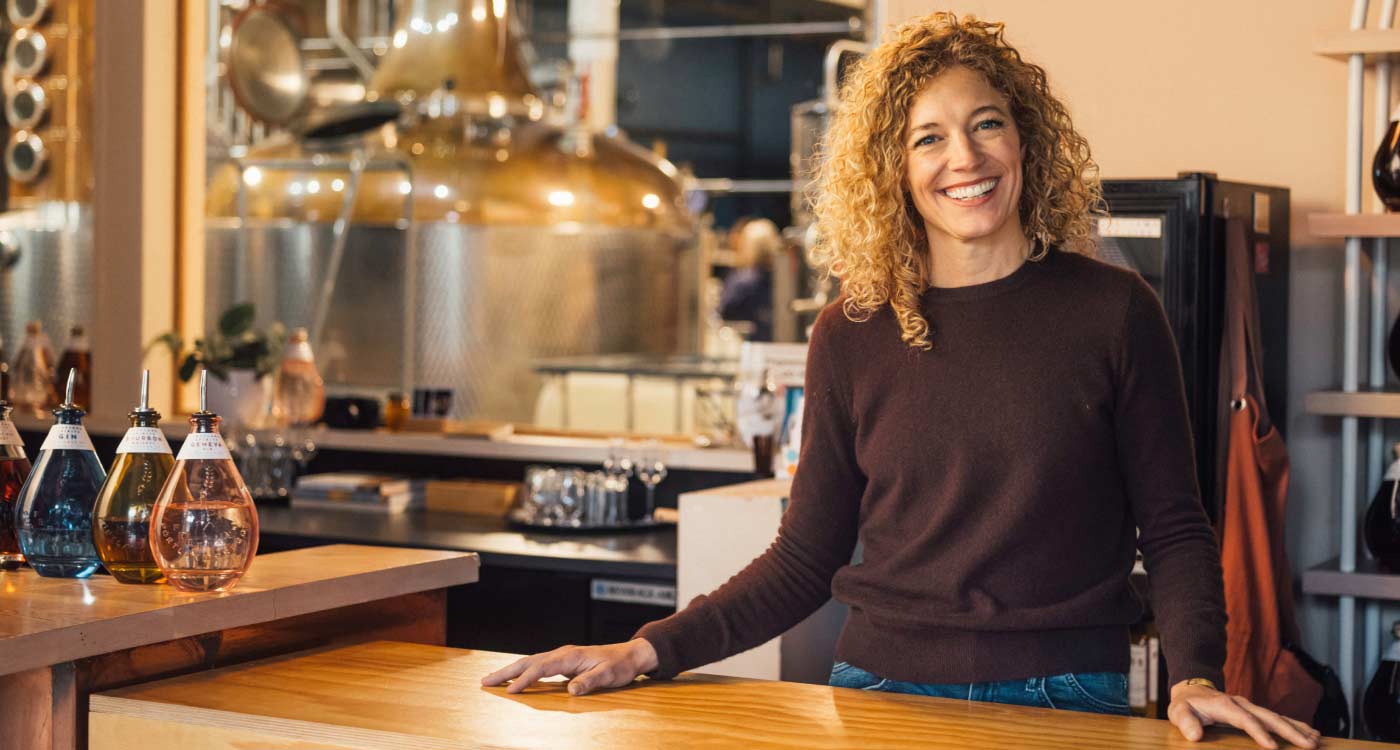 An owner of a spirits manufacturing business is standing in a commercial kitchen and smiling